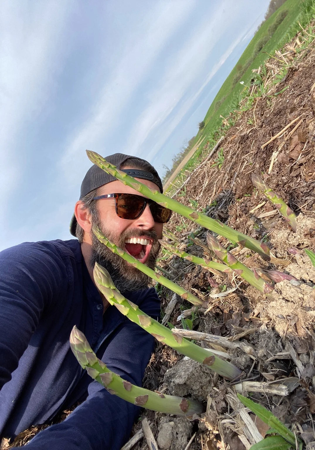 Founder Nick Karnaze smiling on a farm among asparagus