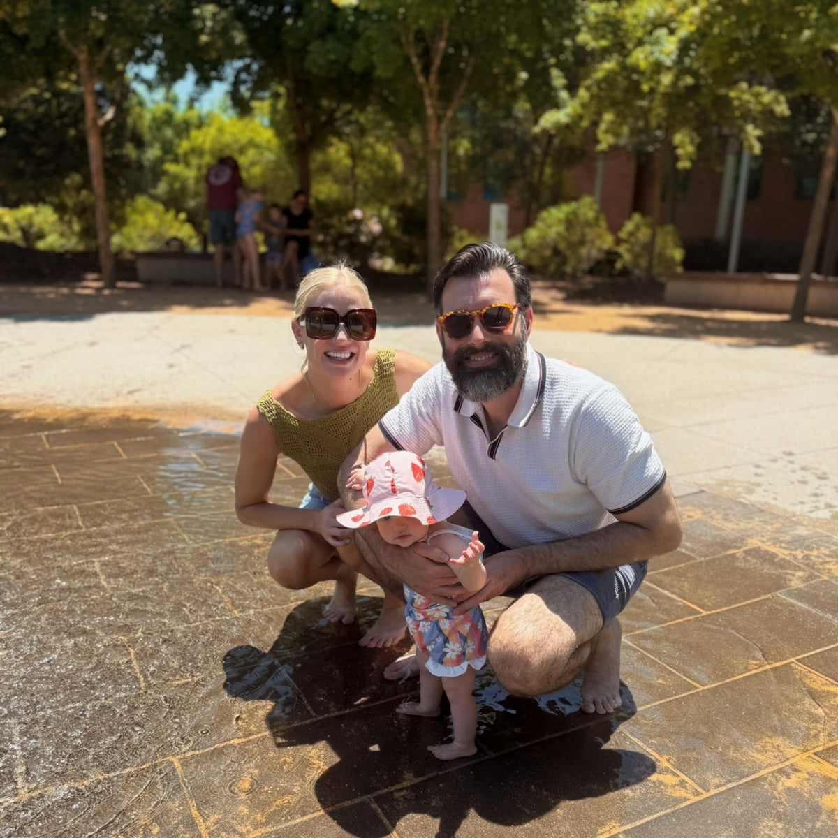 Nick Karnaze crouching at a splash pad with his family on a sunny day